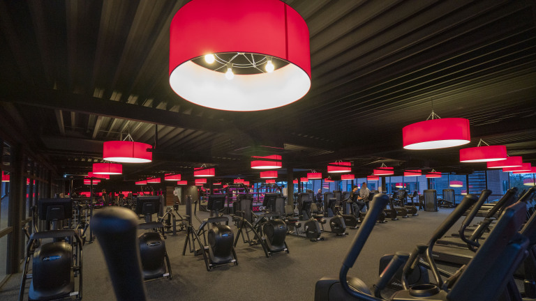 Fitnessruimte met zwarte fitnessapparaten en opvallende rode lampenkappen aan het plafond.