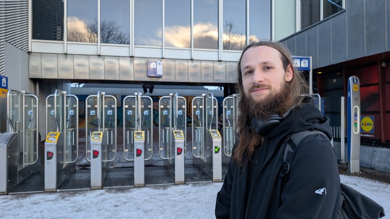 Man met lange baard staat voor poortjes bij een treinstation, die deels gesloten zijn met rode kruizen.