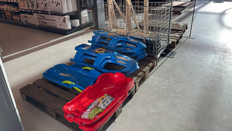 Rode en blauwe sleeën staan uitgestald op houten pallets in een winkel.