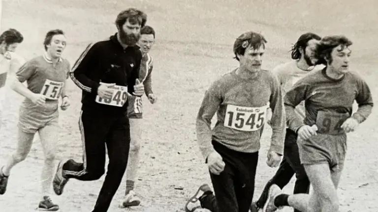 Een groep mensen rent in een wedstrijd, sommigen met startnummers. Het is een zwart-witfoto.