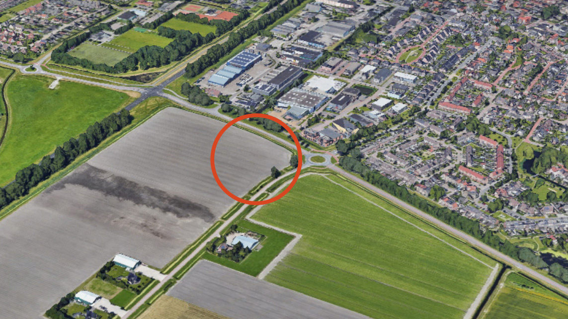 Luchtfoto van een landbouwgebied met een rode cirkel rond het knooppunt van een weg en een rotonde naast gebouwen.
