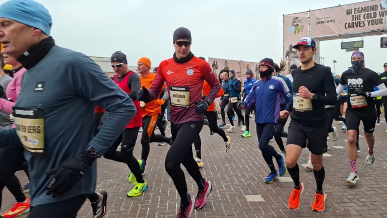Groep hardlopers in sportkleding tijdens een wedstrijd op een bewolkte dag, met starttijd 22 minuten op de achtergrond.