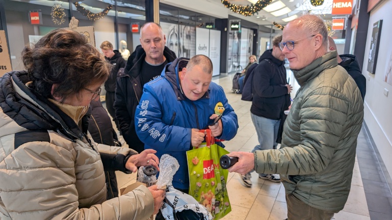 Mensen in een winkelcentrum wisselen voorwerpen uit, omgeven door kerstdecoraties.