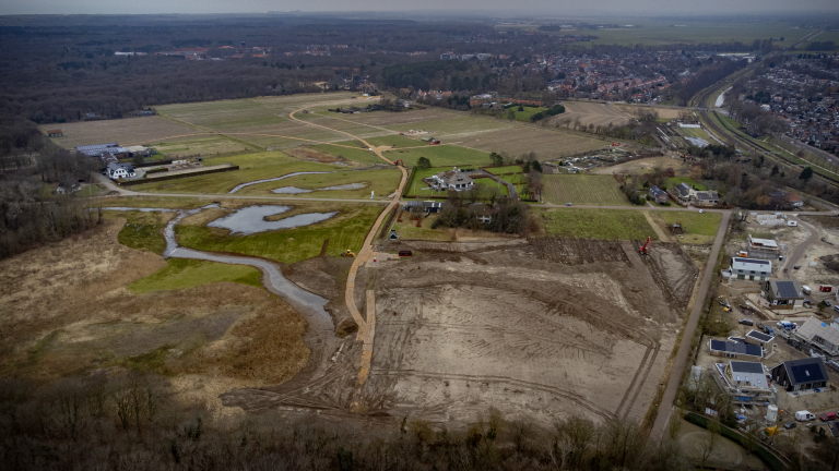 Luchtfoto van een groot landbouwgebied met braakliggend land, een paar huizen, wegen en enkele bouwactiviteiten.