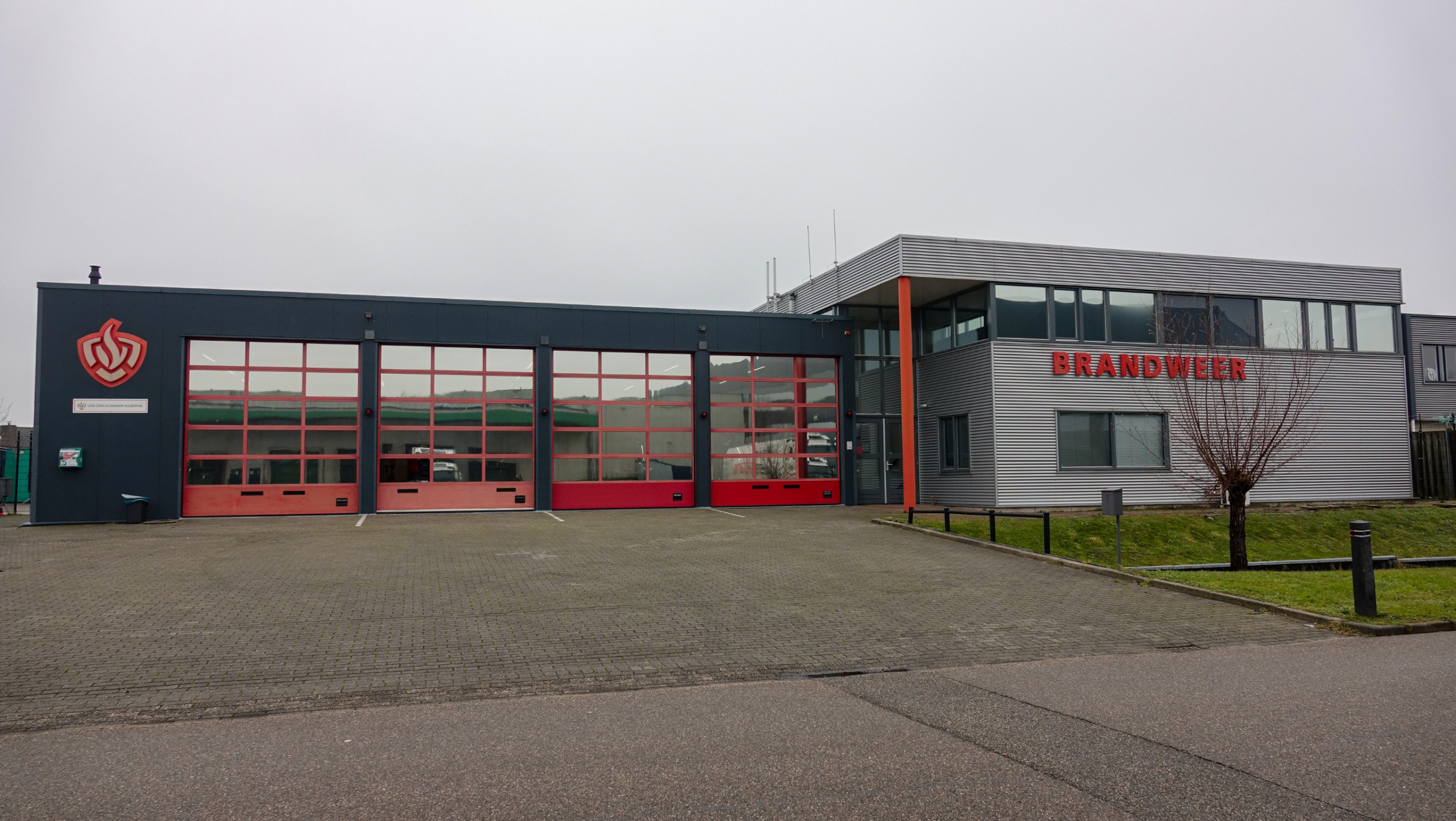 Brandweerkazerne met een grijs gebouw en rode deuren, en het woord "BRANDWEER" in grote rode letters.
