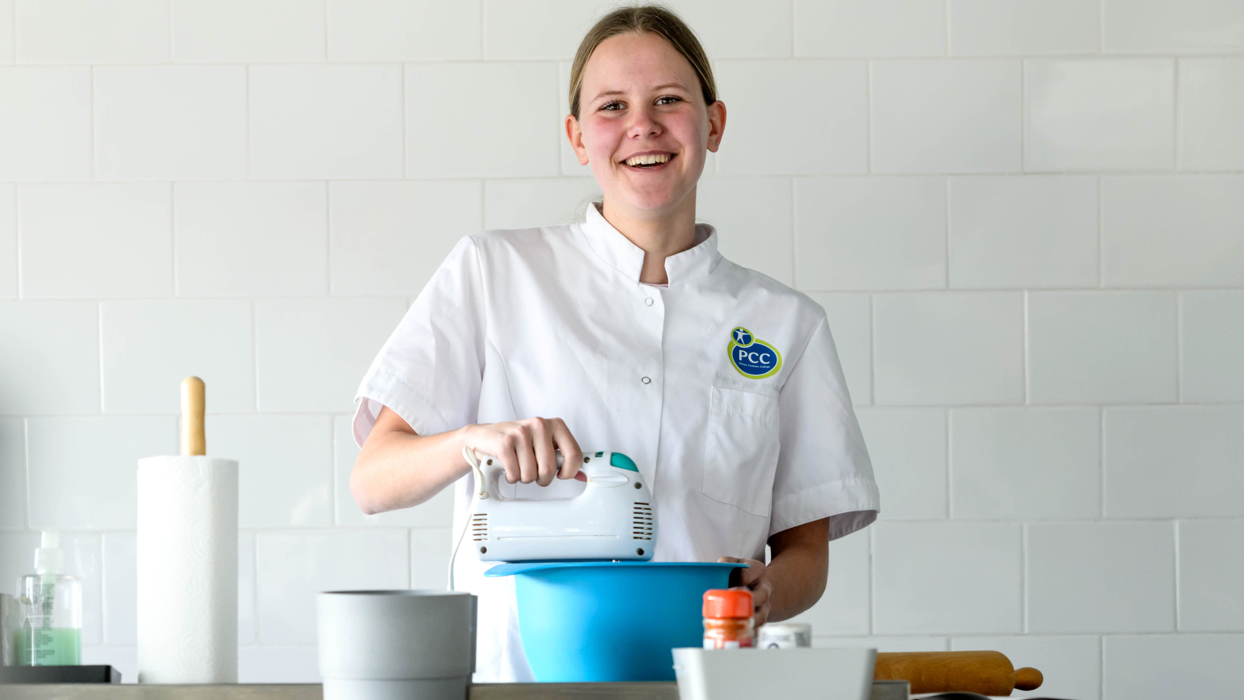 Een jonge vrouw in een witte kokskleding mixt ingrediënten in een blauwe kom in een keuken.