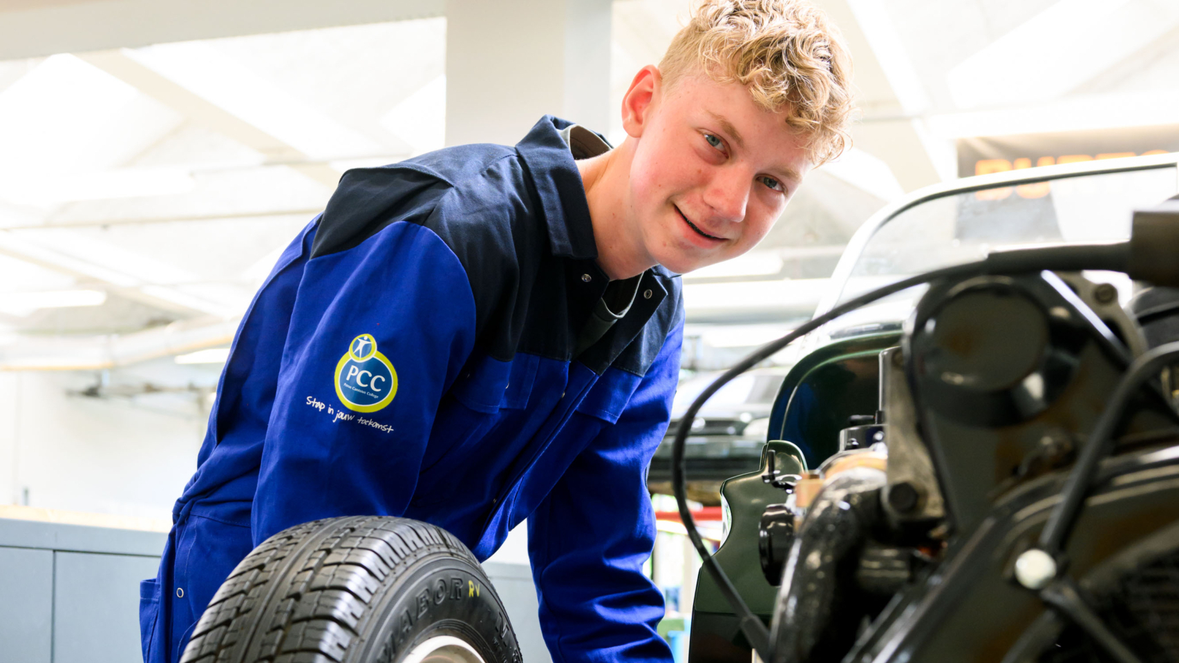 Een jonge man in blauwe overall werkt aan een wiel in een autowerkplaats.
