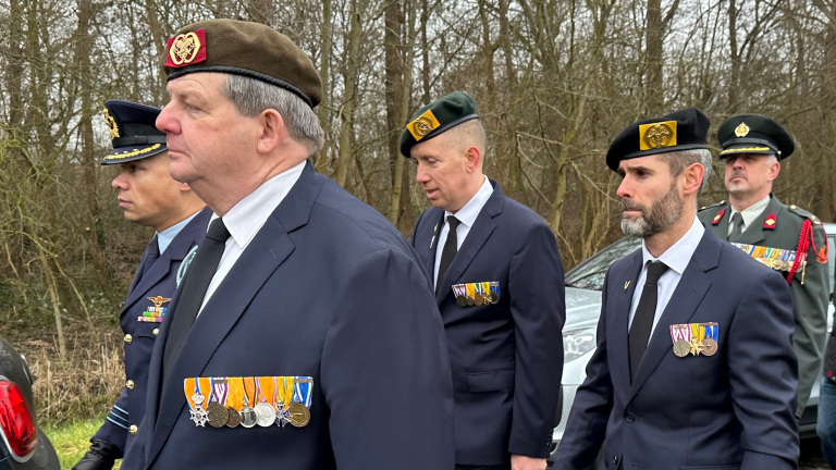 Mannen in uniformen dragen medailles en marcheren naast elkaar in een bosrijke omgeving.