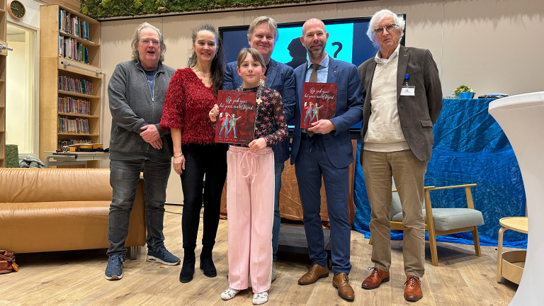 Zes mensen poseren binnen in een ruimte, twee van hen houden boeken vast met de titel "Op zoek naar het spoor van...".