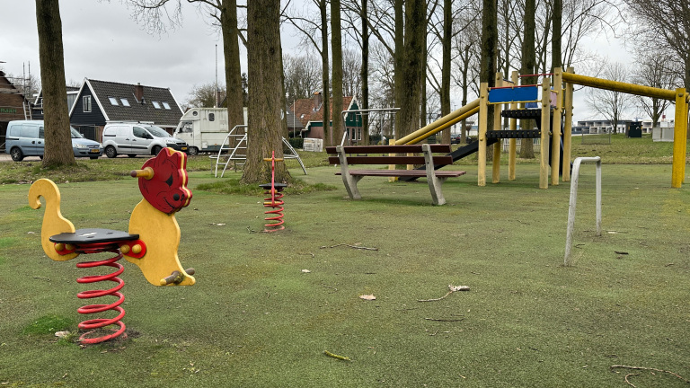 Speeltuin met speeltoestellen zoals een wipkip in de vorm van een kat, glijbaan, en een bankje, omgeven door bomen.