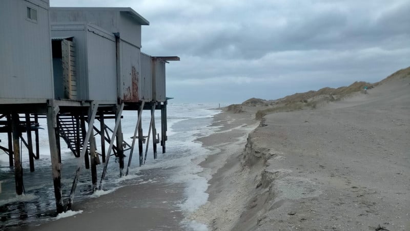 Stiltgebouw op een verlaten strand met woeste zee en dreigende wolken boven.