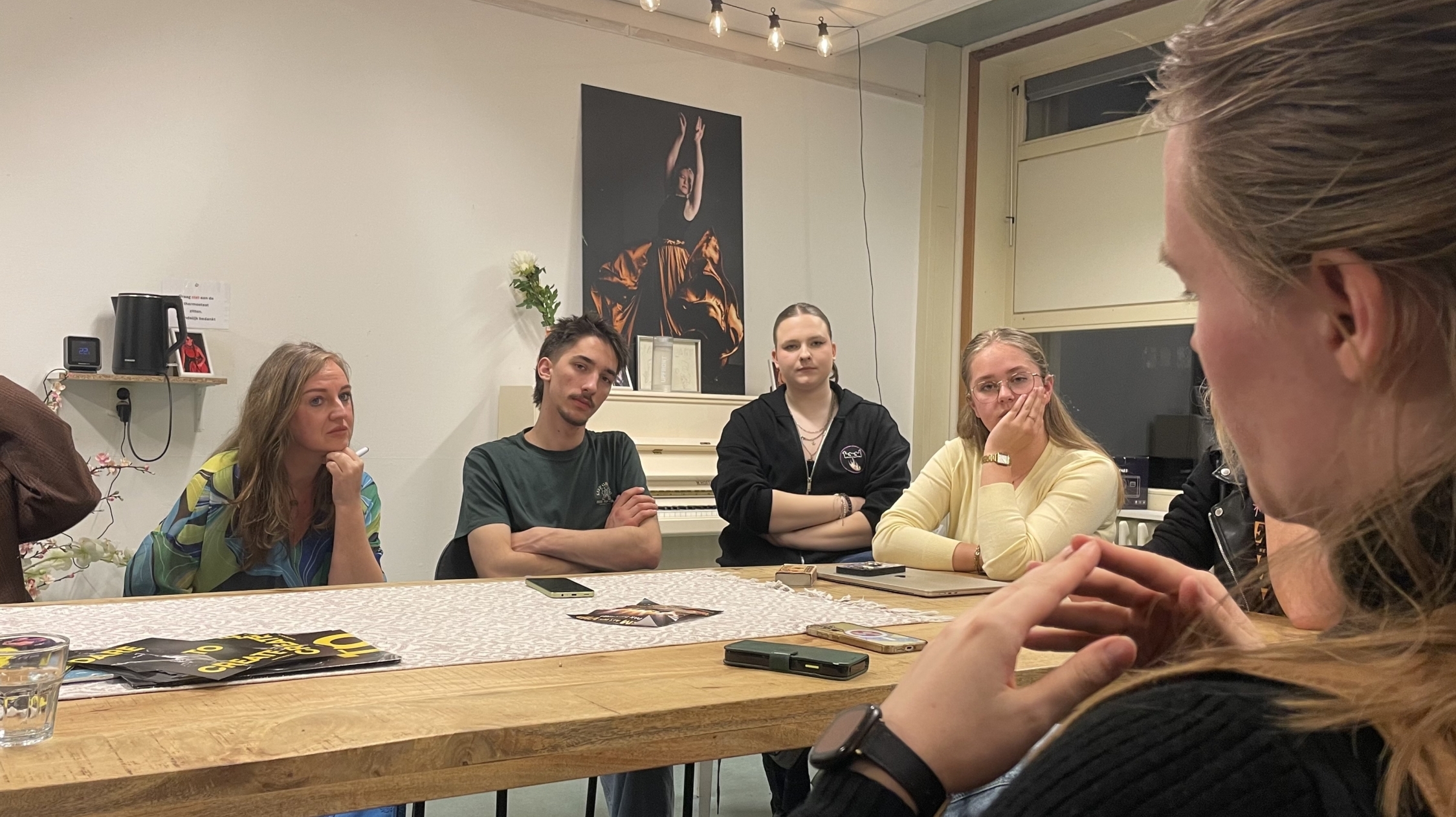 Een groep mensen zit rond een tafel in een vergaderruimte en luistert aandachtig naar een spreker buiten beeld.