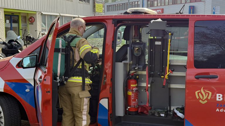Brandweerman in uitrusting bij een geopende brandweerwagen met apparatuur en brandblusser binnenin.