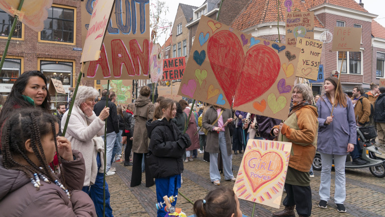 Mensen op een protestmars dragen kleurrijke borden met hartjes en teksten zoals "Girl Power" en "Nee is Nee".