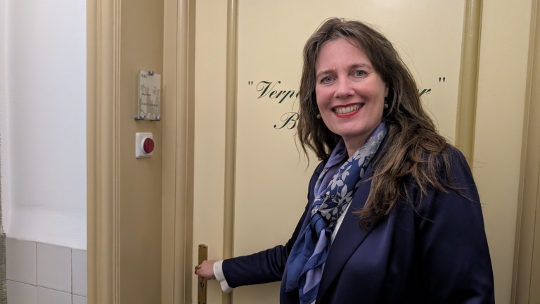 Vrouw met donkerblauwe blazer en sjaal opent een deur met de tekst "Verpleegkundige Bespreekkamer".