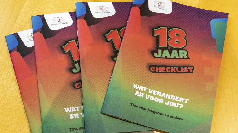 Drie kleurrijke brochures met de tekst "18 Jaar Checklist" van de gemeente Alkmaar op een houten tafel.