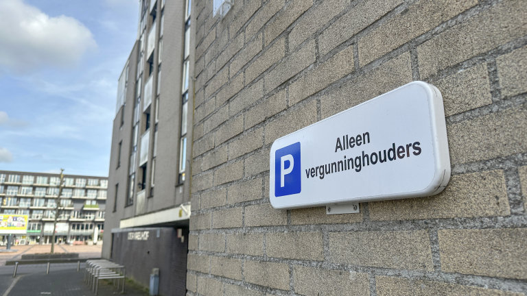 Parkeerbord aan een bakstenen muur met de tekst "Alleen vergunninghouders" naast een flatgebouw.