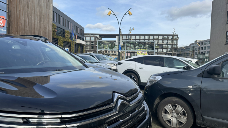 Gewoon parkeerplaats met diverse auto's op een zonnige dag, naast moderne gebouwen waaronder een bibliotheek.