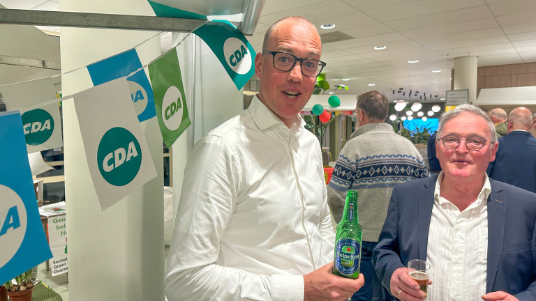 Twee mannen op een feest met CDA-vlaggetjes, één houdt een Heineken 0.0-fles vast.