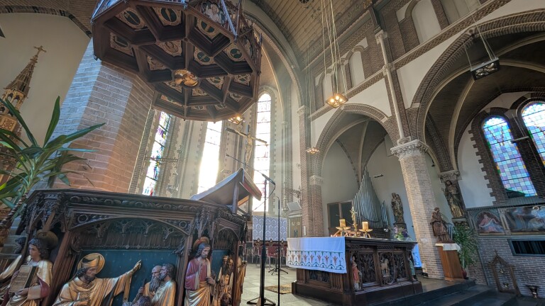 Interieur van een kerk met een rijkelijk versierd preekgestoelte, gebrandschilderde ramen en een altaar met crucifix.
