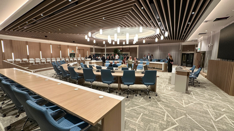 Vergaderruimte met ronde tafels, blauwe stoelen en hanglampen, waar mensen zich informeel verzamelen.