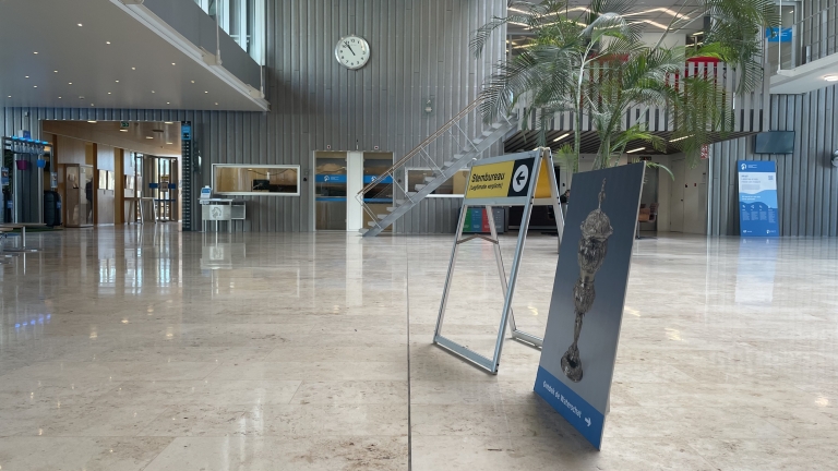 Binnenruimte met een stemlokaalbord en een klok boven een trap, omgeven door moderne interieurdecoratie en planten.