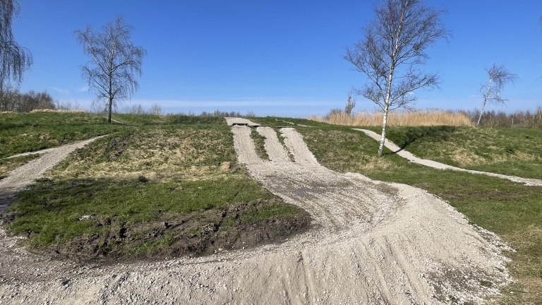 Kronkelende zandpaden op een heuvelachtig terrein met kale bomen onder een heldere blauwe lucht.