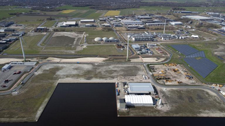 Industrieel landschap met windturbines, zonnepaneelvelden, en gebouwen omringd door groene en bebouwde gebieden.