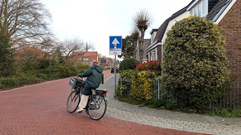 Persoon op een fiets rijdt op een roodbruine straat langs een bord met "uitgezonderd fietsers" in een rustige woonwijk.