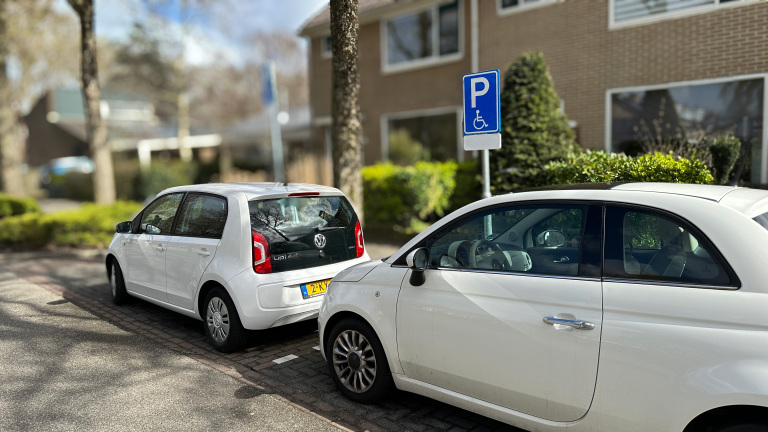 Twee witte auto's geparkeerd naast een bord voor gehandicaptenparkeerplaatsen in een rustige woonwijk.
