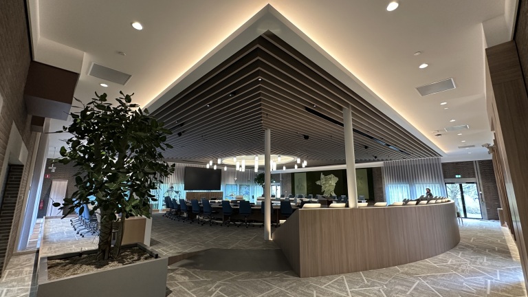 Moderne vergaderruimte met een grote tafel in het midden, blauwe stoelen, hangende lampen en een decoratief plafond met houten panelen.