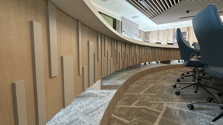 Binnenkant van een moderne vergaderruimte met een gebogen houten wanddecoratie en blauwe bureaustoelen op een tapijtplavijsel.