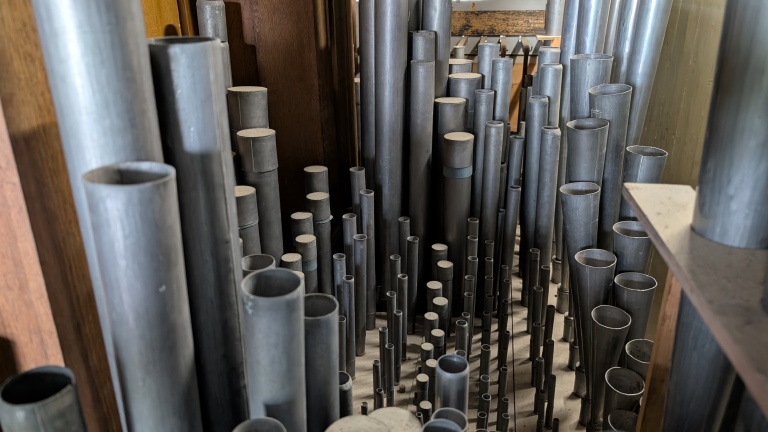 Een verzameling pijporgelpijpen in verschillende lengtes en diktes, opgesteld in een houten kast.