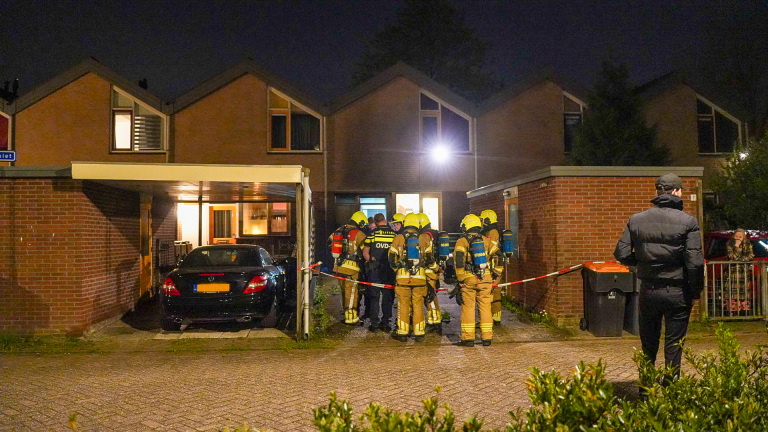 Brandweerlieden in uitrusting staan bij een huis met een zwarte auto onder een carport, afgezet met rood-wit lint.