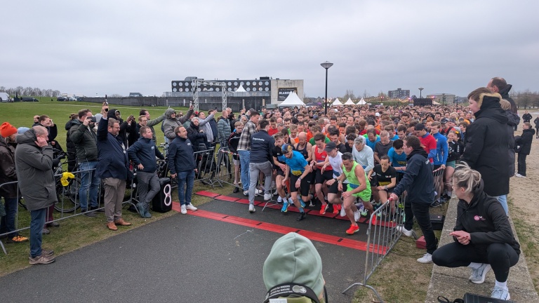 Een menigte hardlopers staat klaar aan de startlijn van een race, omringd door toeschouwers en organisatoren.