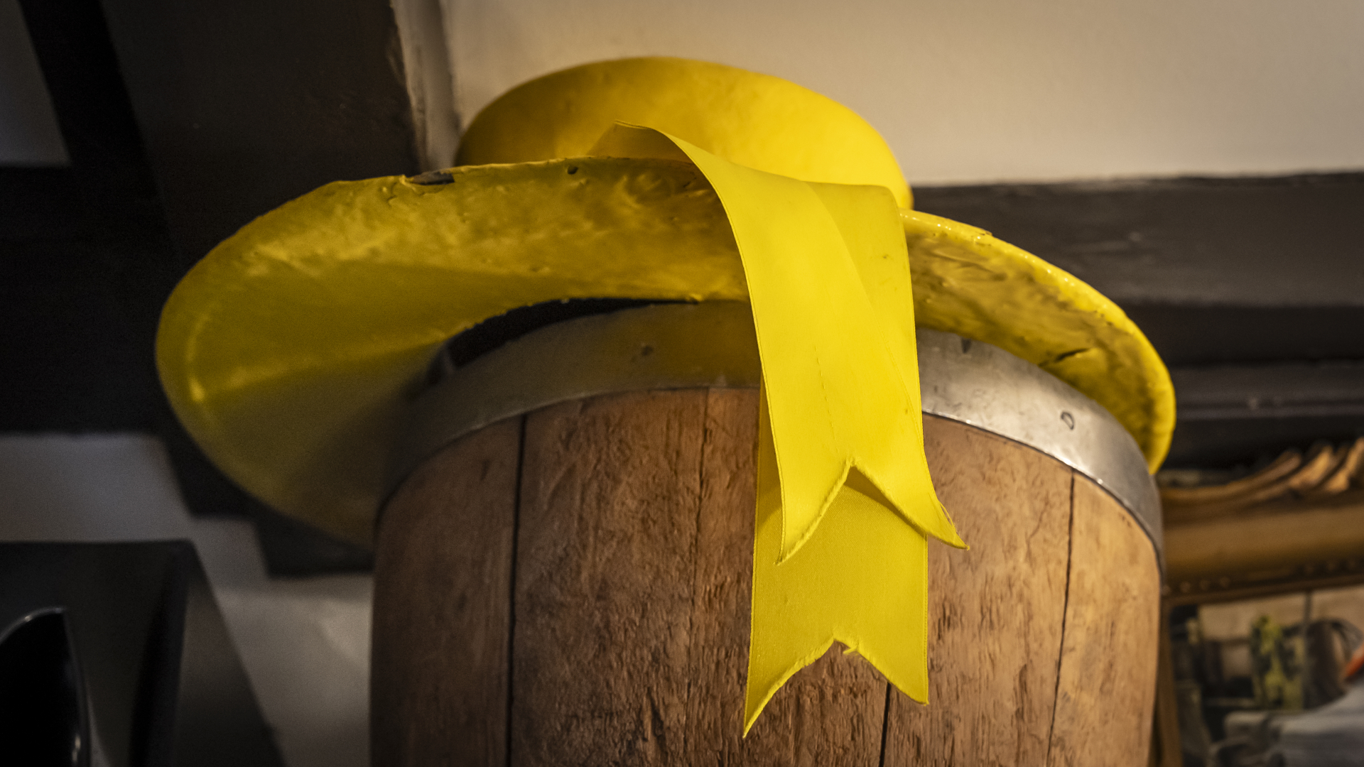 Gele hoed met lint op een houten vat, waarbij het lint naar beneden hangt.