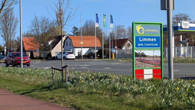 Bord bij een rotonde met "Limmen gem. Castricum" en afbeeldingen van bloemen. Op achtergrond huizen en een tankstation.