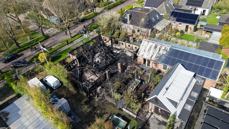Uitgebrande woning in een woonwijk, omringd door onbeschadigde huizen met zonnepanelen.