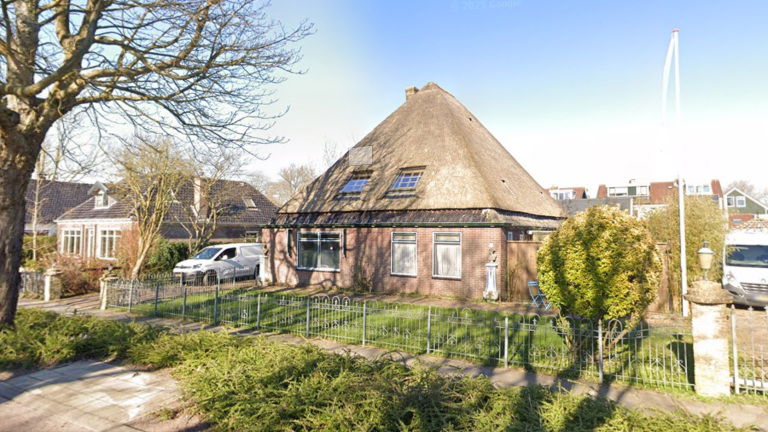 Een huis met rieten dak en bakstenen muren, omgeven door een hek met groen eromheen en een bestelbus op de oprit.