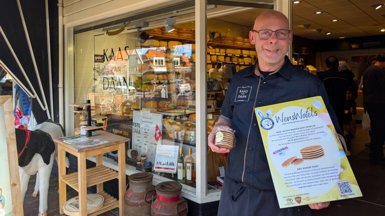 Winkelmedewerker voor een kaaswinkel houdt een bord vast met informatie over WensWafels voor een goed doel.