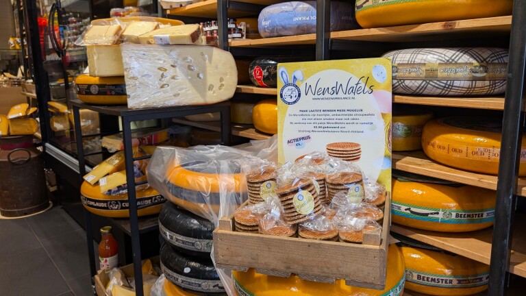 Een winkel met een rek vol kaaswielen, een kraam met verpakte stroopwafels en een bord met informatie over WensWafels.