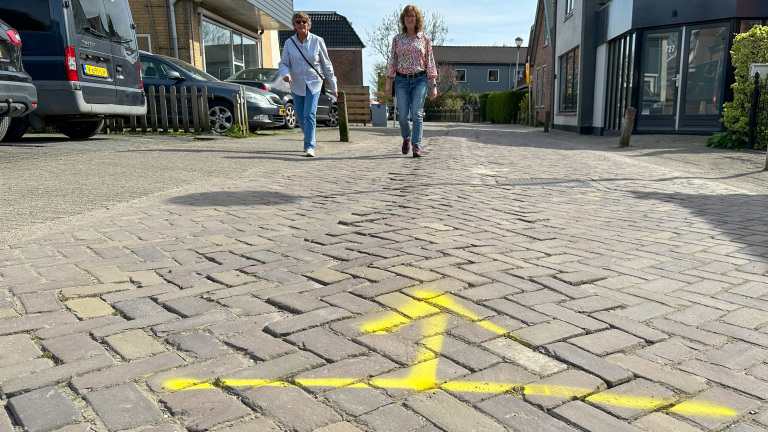 Twee mensen wandelen op een met stenen geplaveide straat met een gele pijl op de grond.
