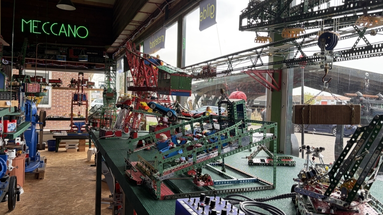 Een tafereel met Meccano-modellen in een zonovergoten tentoonstelling met verschillende complex geconstrueerde structuren en machines.