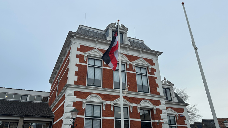 Rood bakstenen gebouw met witte accenten, een vlag met zwarte, rode en witte banen, en het jaartal 1895 op de gevel.