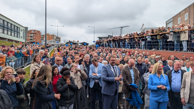 Een grote menigte mensen staat buiten, enkele nemen foto's tijdens een openbare bijeenkomst.
