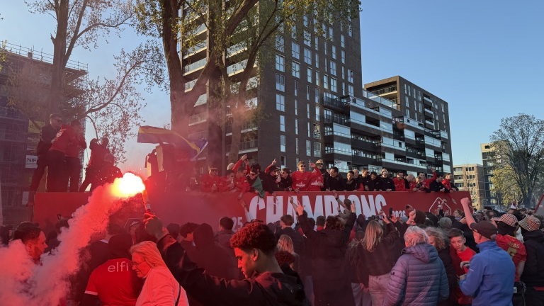 Mensen vieren feest op straat met rookbommen en een groot bord met de tekst "CHAMPIONS" op de achtergrond.