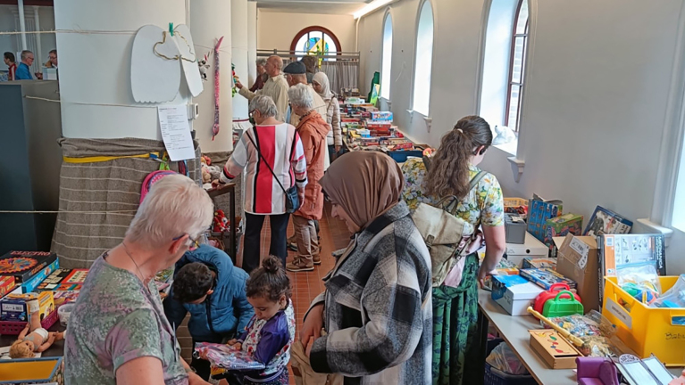 Mensen bekijken speelgoed en spelletjes op tafels in een lichte ruimte met gebogen ramen.