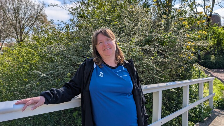 Vrouw glimlacht terwijl ze leunt tegen een witte railing, met een groene struik op de achtergrond.