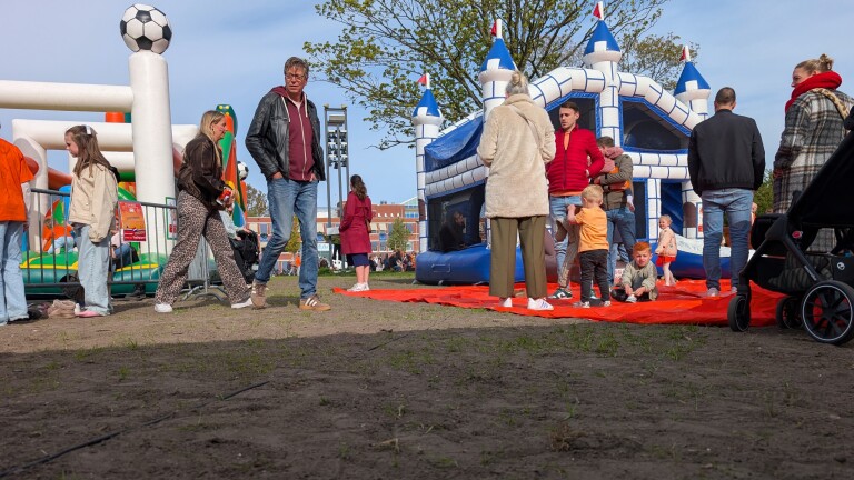 Mensen staan bij springkussens in de vorm van kasteel en voetbal op een buitenevenement, met een kinderwagen op de voorgrond.