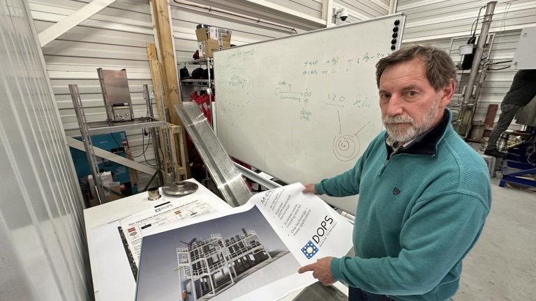 Een man in een werkplaats toont een poster van een industrieel ontwerp naast een volgeschreven whiteboard.